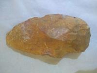 an orange coloured paleolithic handaxe lies against a white background
