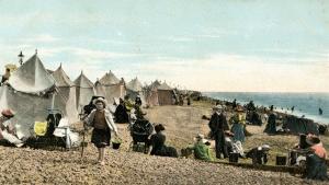 A colourised postcard image showing bathing tents lined up along Littlehampton Beach circa 1920s. People are enjoying the beach and the water.